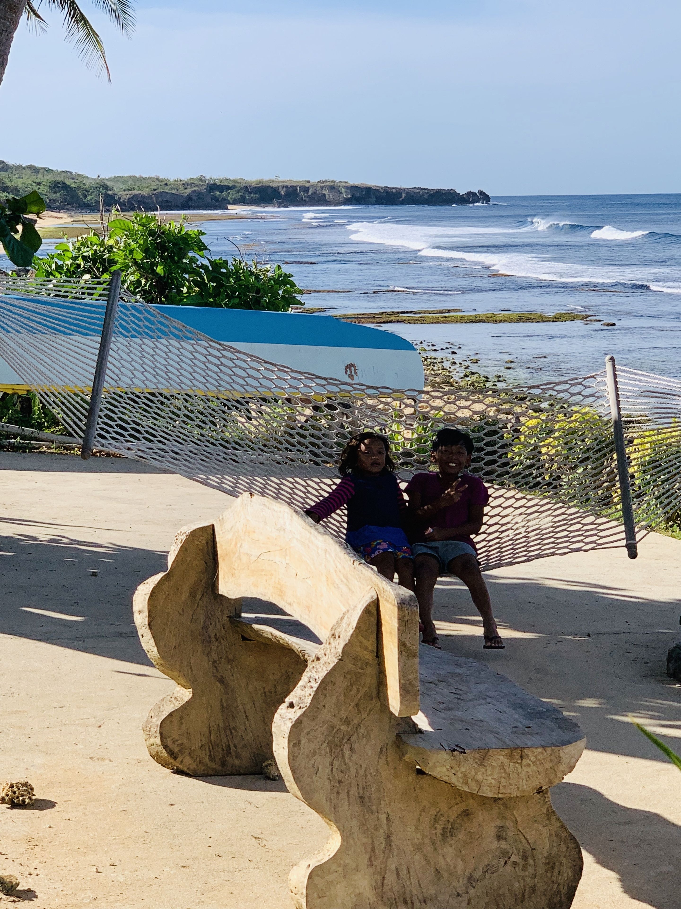 A beach scene with a concrete sculpture, a blue and white surfboard, and a netted area.