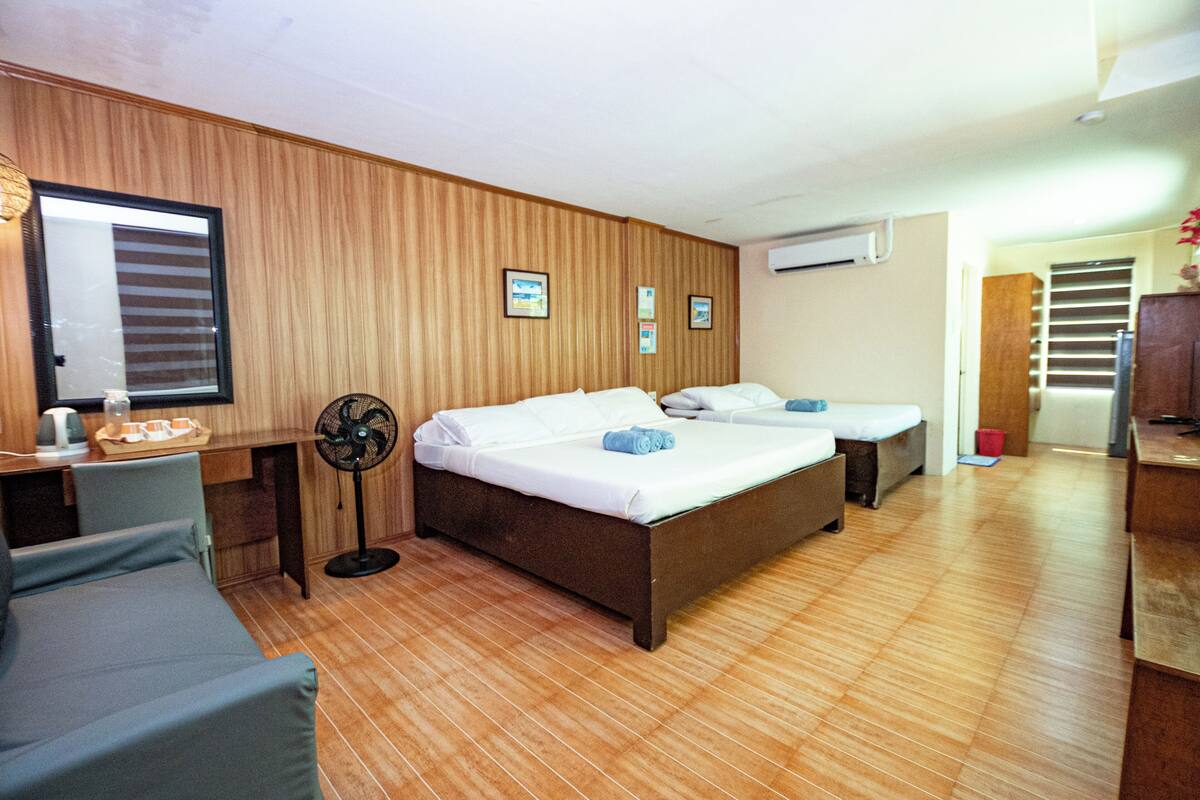 Ein Hotelzimmer mit zwei Betten, Holzboden, Schreibtisch mit Ventilator und Spiegel.
