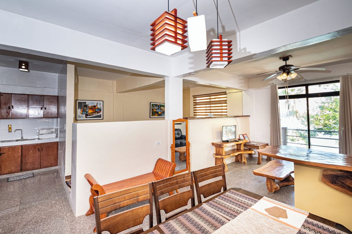 Ein modernes Wohnzimmer mit Essbereich, Holzmöbeln, einem Deckenventilator und einem großen Fenster.