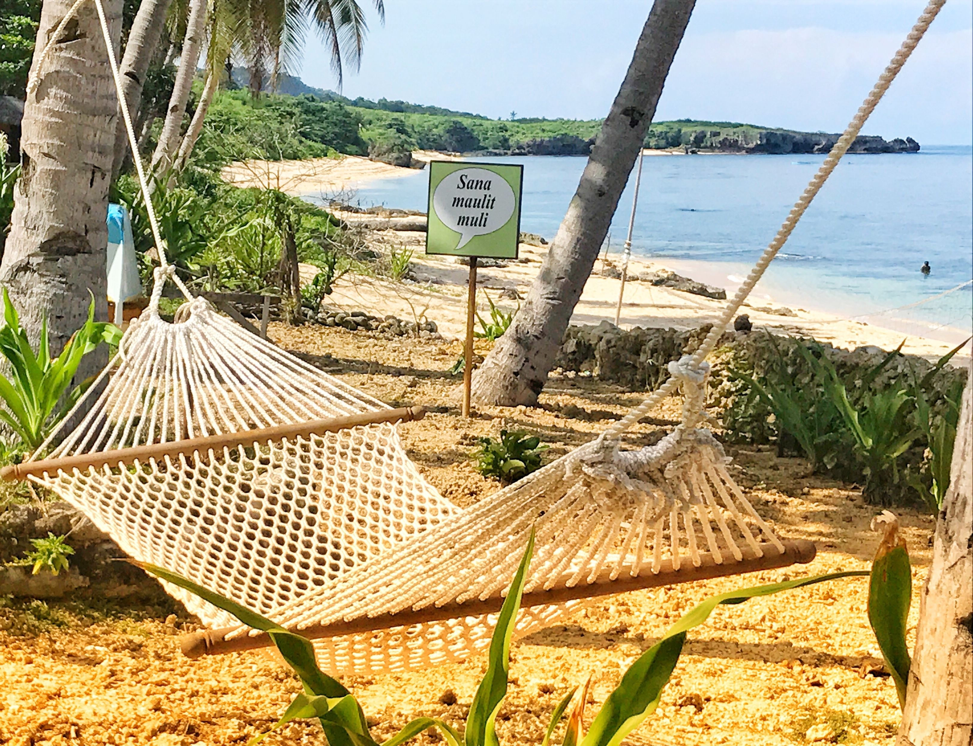 Una hamaca sobre una playa arenosa con un cartel al fondo.
