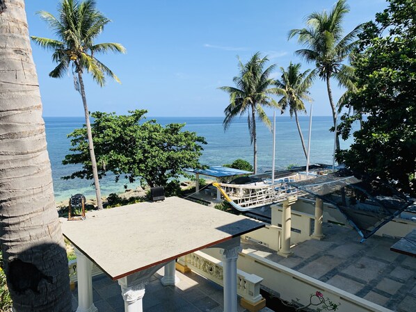 Vista de la playa con palmeras, piscina y un pabellón con vistas al océano.