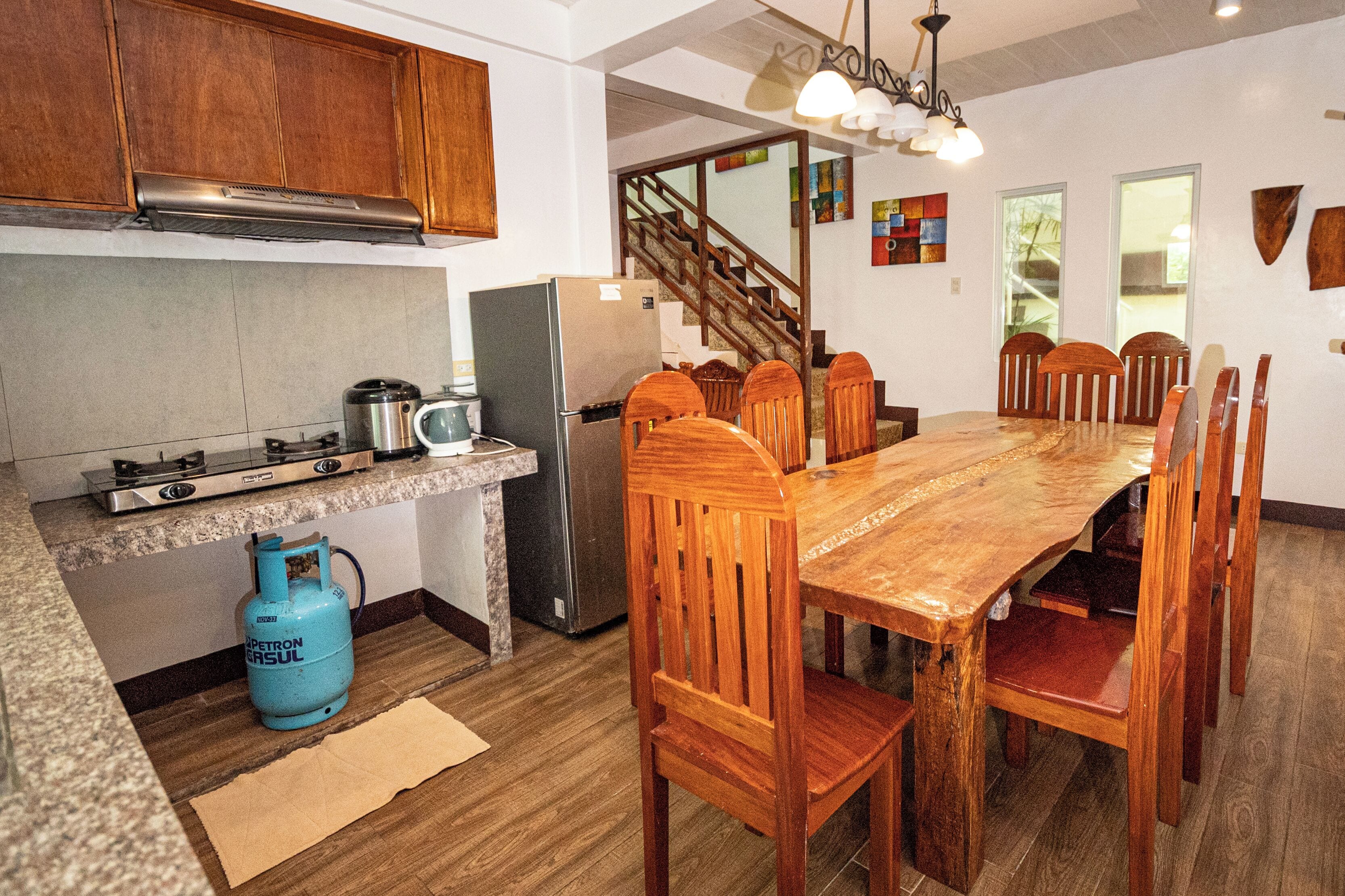 Cocina con estufa a gas, refrigerador y mesa de madera con sillas.