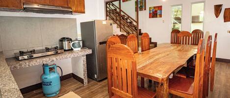 Cocina con estufa a gas, refrigerador y mesa de madera con sillas.