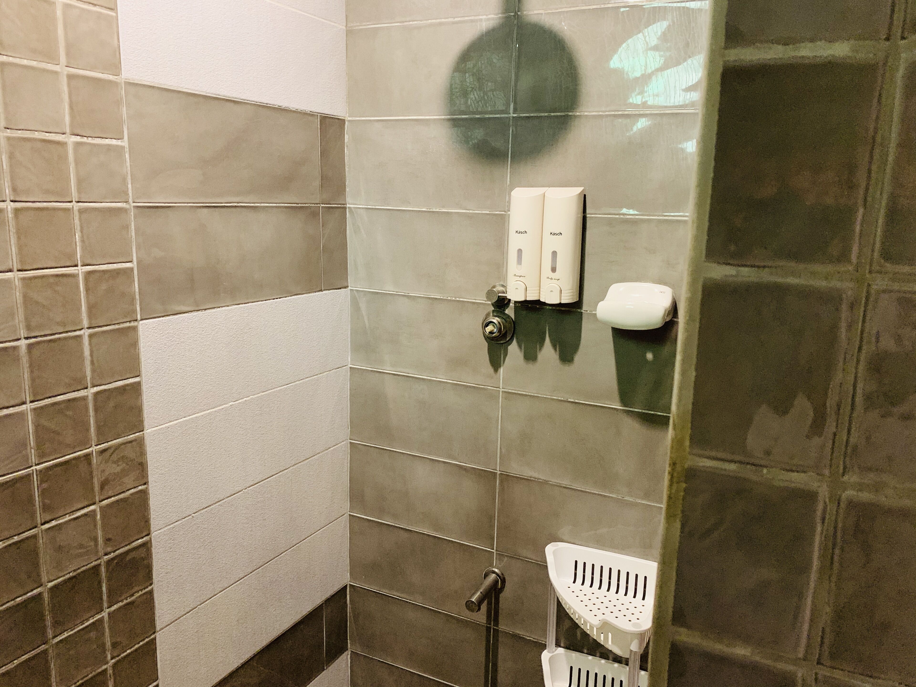 A bathroom with tiled walls, a hand dryer, and a soap dispenser.