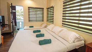 A hotel room with two beds, a TV, and large windows with blinds.