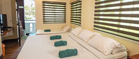 Quarto de hotel com duas camas, televisão e janelas amplas com persianas.