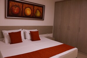 A hotel room with a bed, two pillows, a red throw blanket, and a painting of fruits on the wall. - Apartasuites La Flora (Cali)