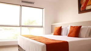 A hotel room with a large bed, white bedding, and orange throw pillows. - Apartasuites La Flora (Cali)