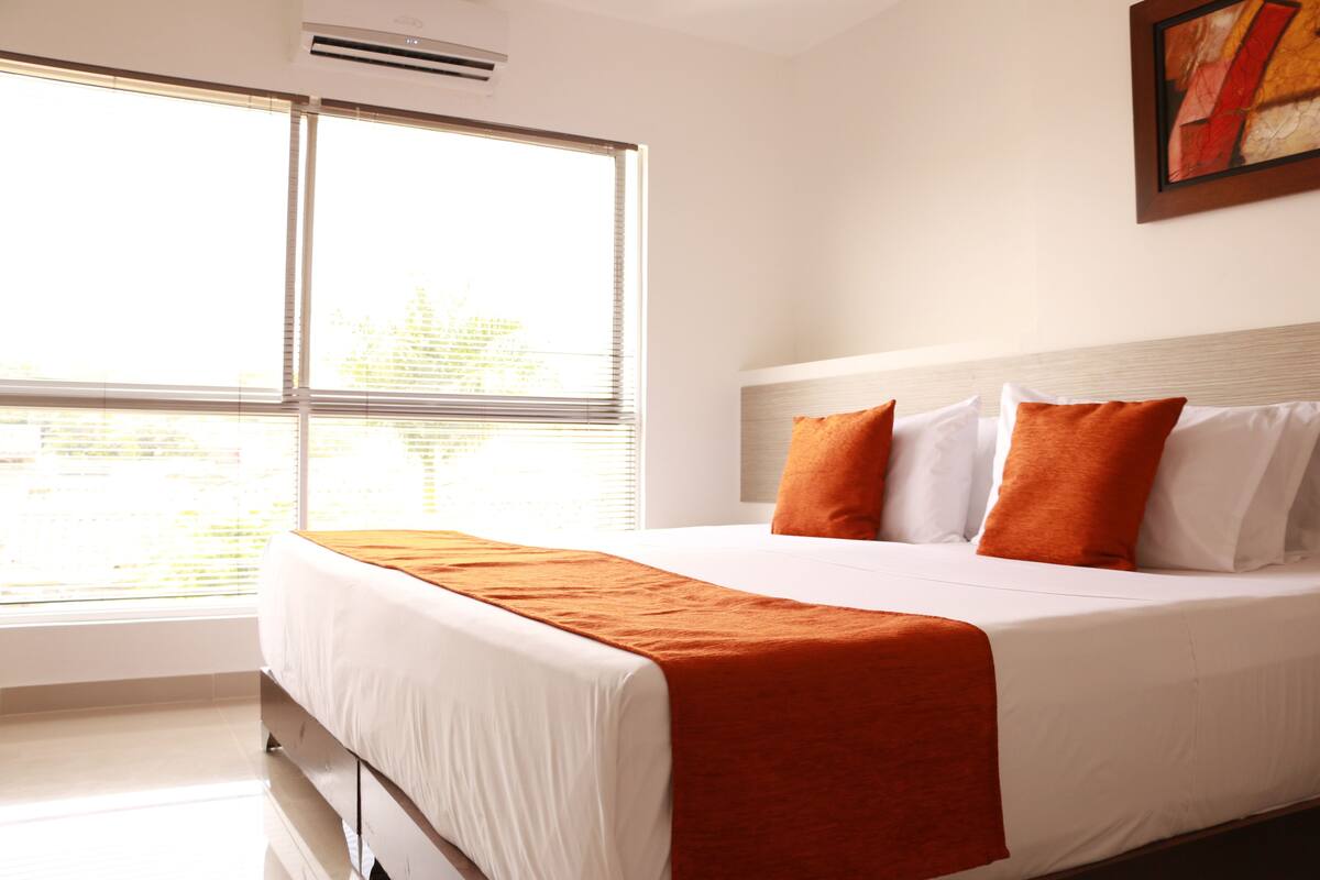 A hotel room with a large bed, white bedding, and orange throw pillows.