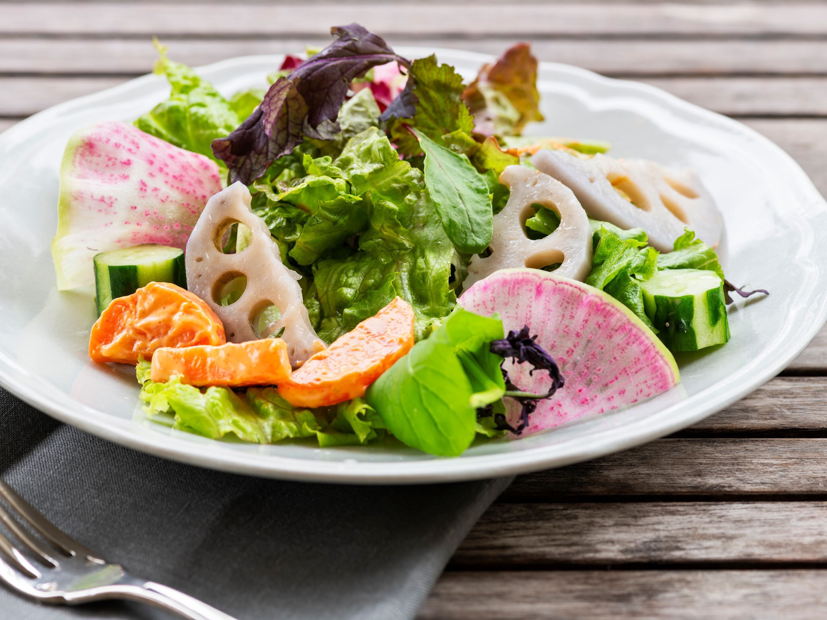 A plate of mixed greens and vegetables on a wooden table.