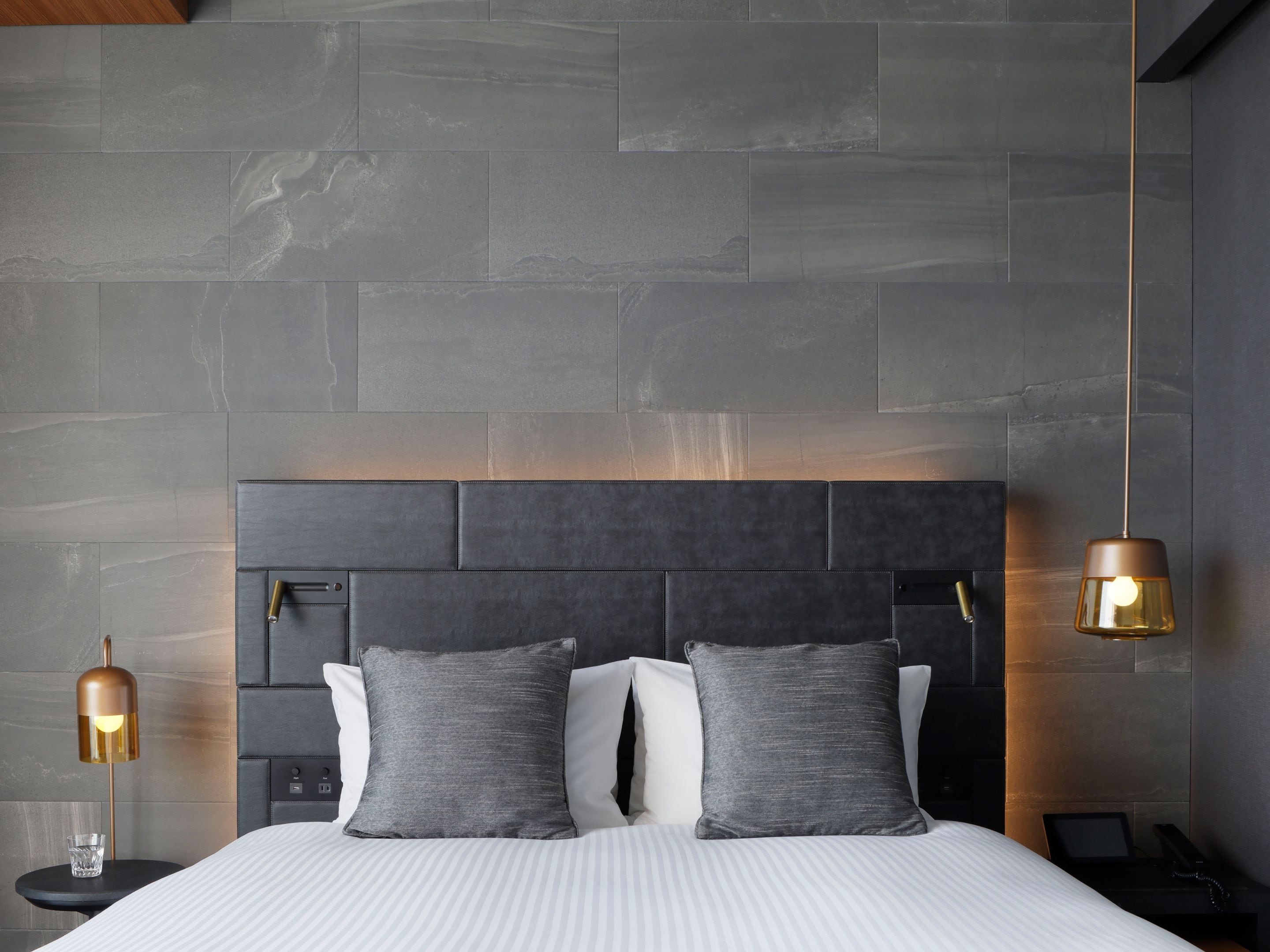 A modern bedroom with a large bed, a headboard, bedside tables, and a hanging light fixture.
