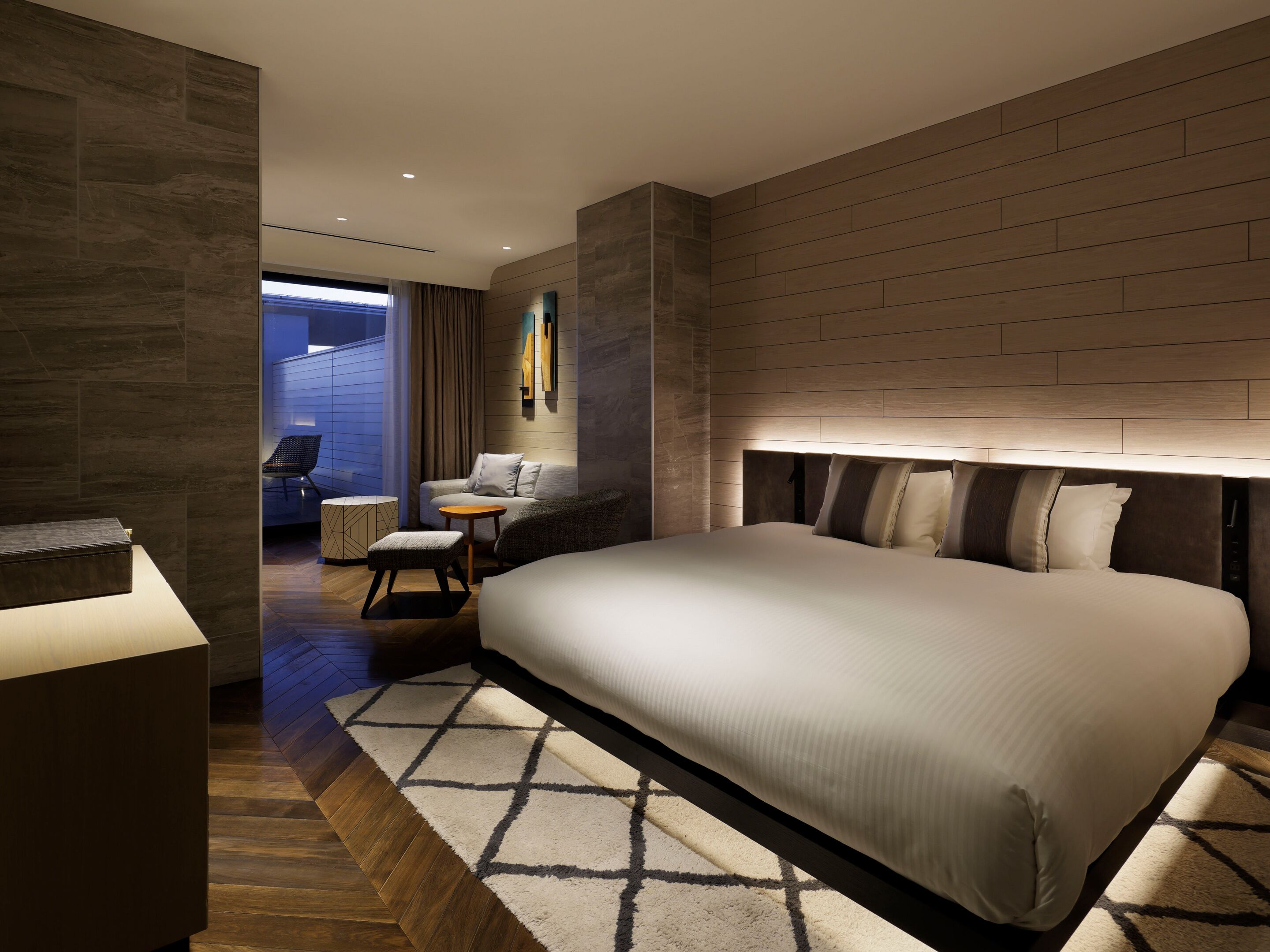 Habitación de hotel moderna con una cama grande, una zona de estar con una mesita y vistas al exterior.