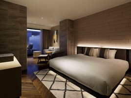 A modern hotel room with a large bed, a seating area with a small table, and a view of the outside.