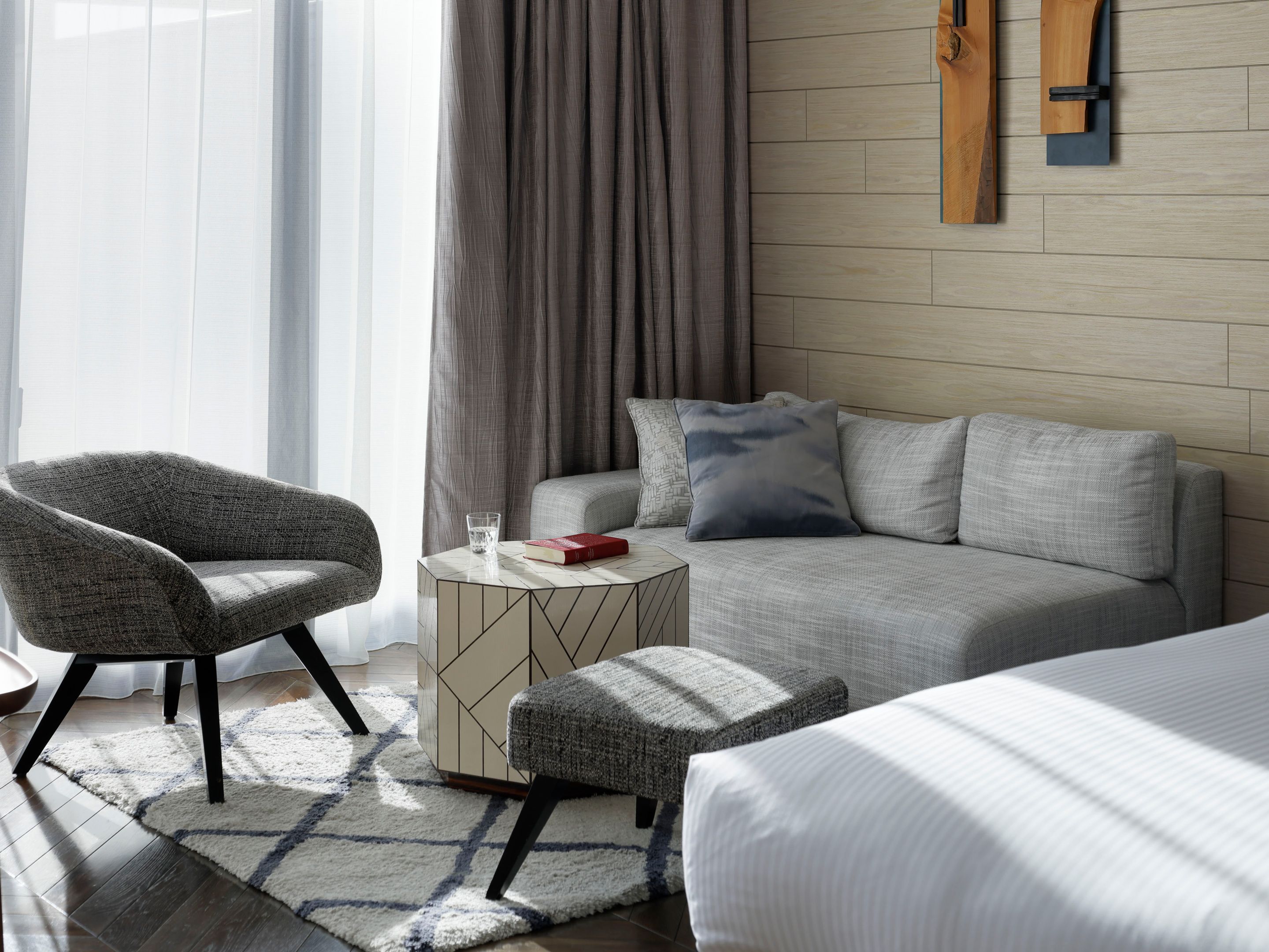 Quarto de hotel moderno com sofá, poltrona, banqueta e cama.