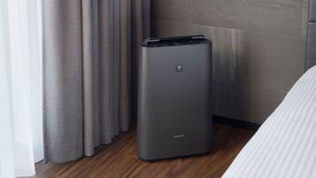 A room with a grey trash bin labeled 'SHARP' and a bed with white bedding.