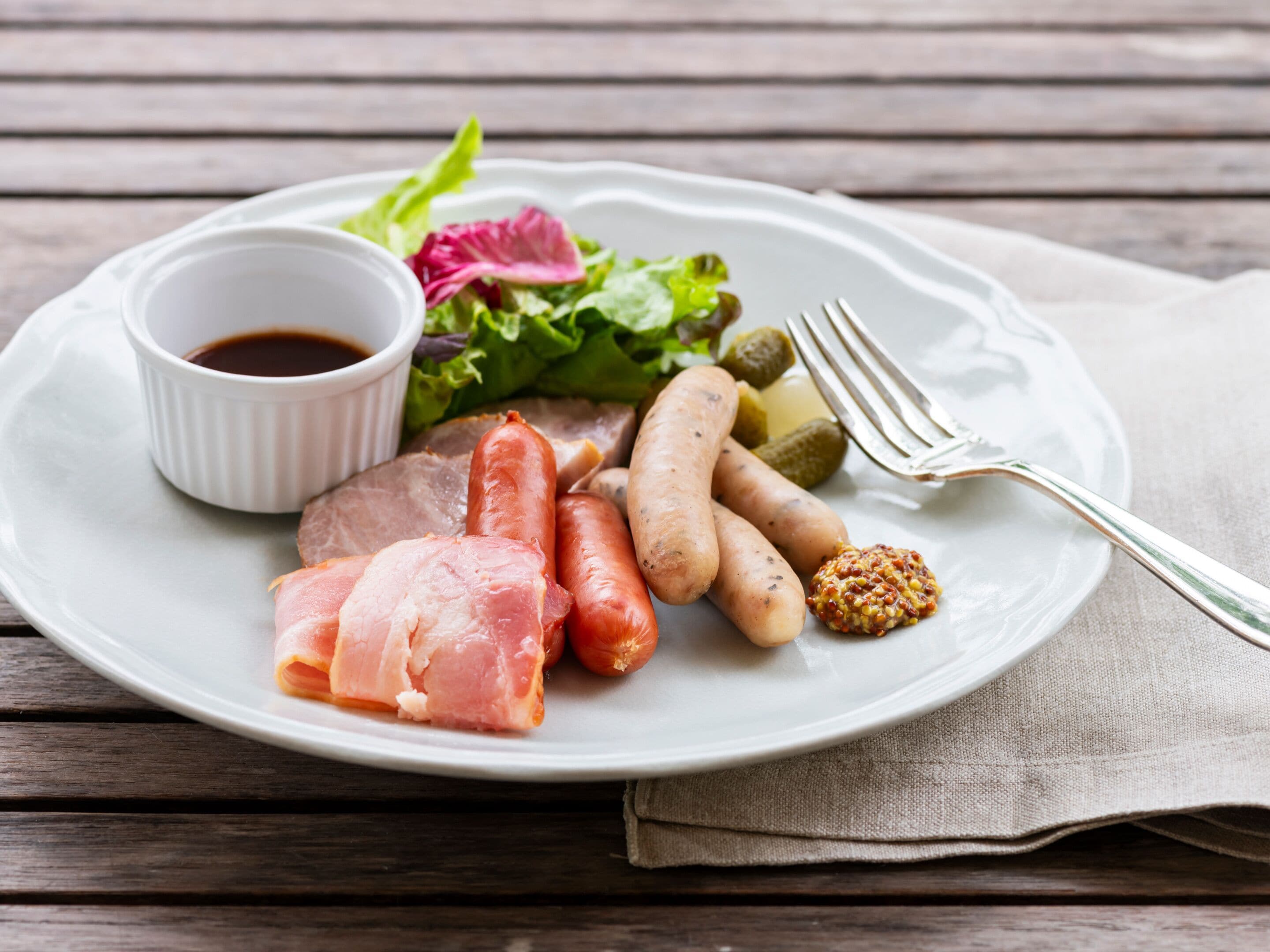 Un plato con varias carnes, encurtidos y un recipiente pequeño con salsa sobre una mesa de madera.