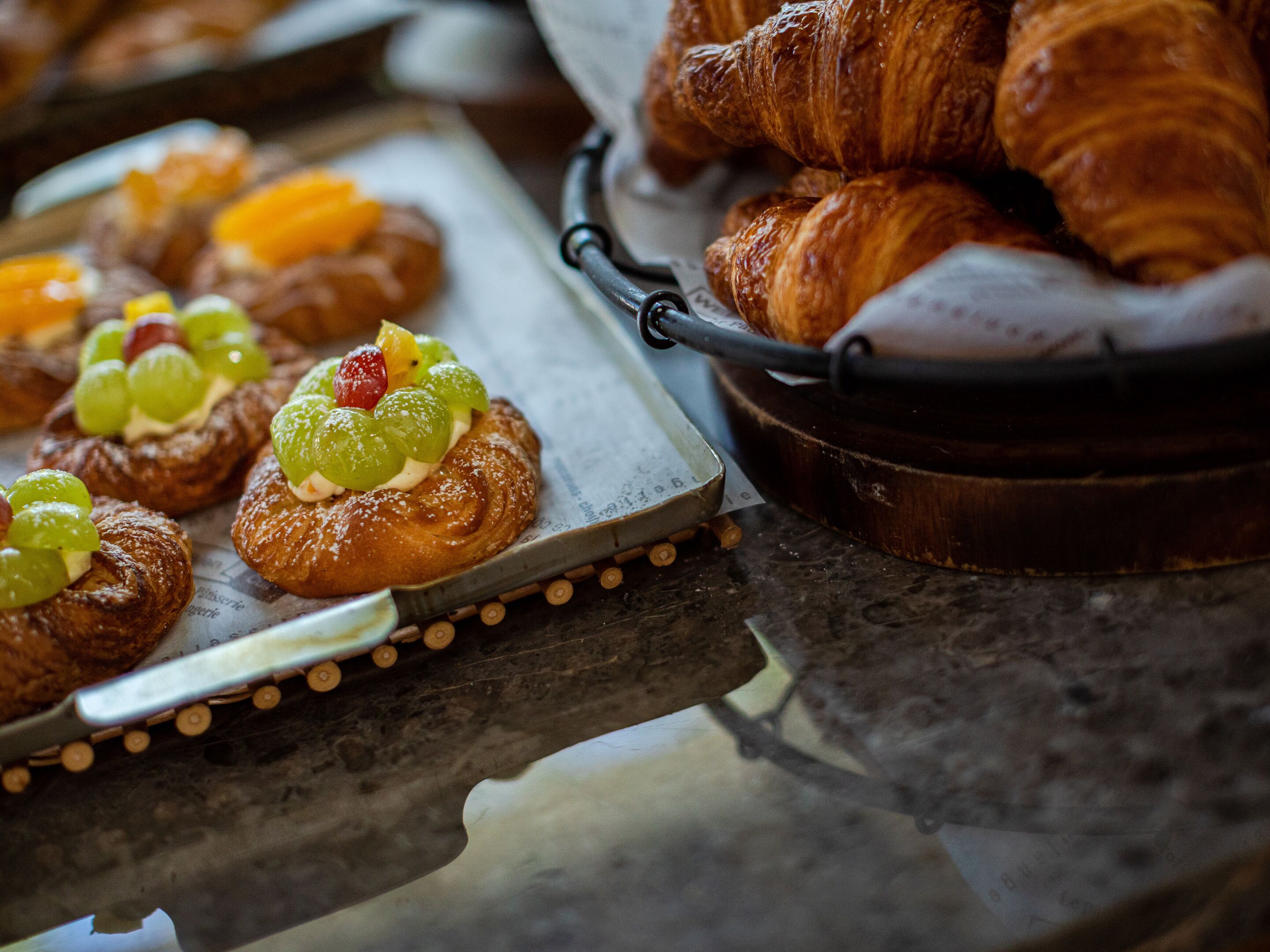 A tray of pastries with fruit toppings and a basket of croissants.