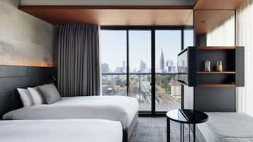 A modern hotel room with two beds, a small table, a TV, and a city view.