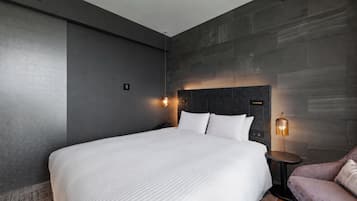 A modern hotel room with a large bed, a small seating area, and a wall-mounted headboard.