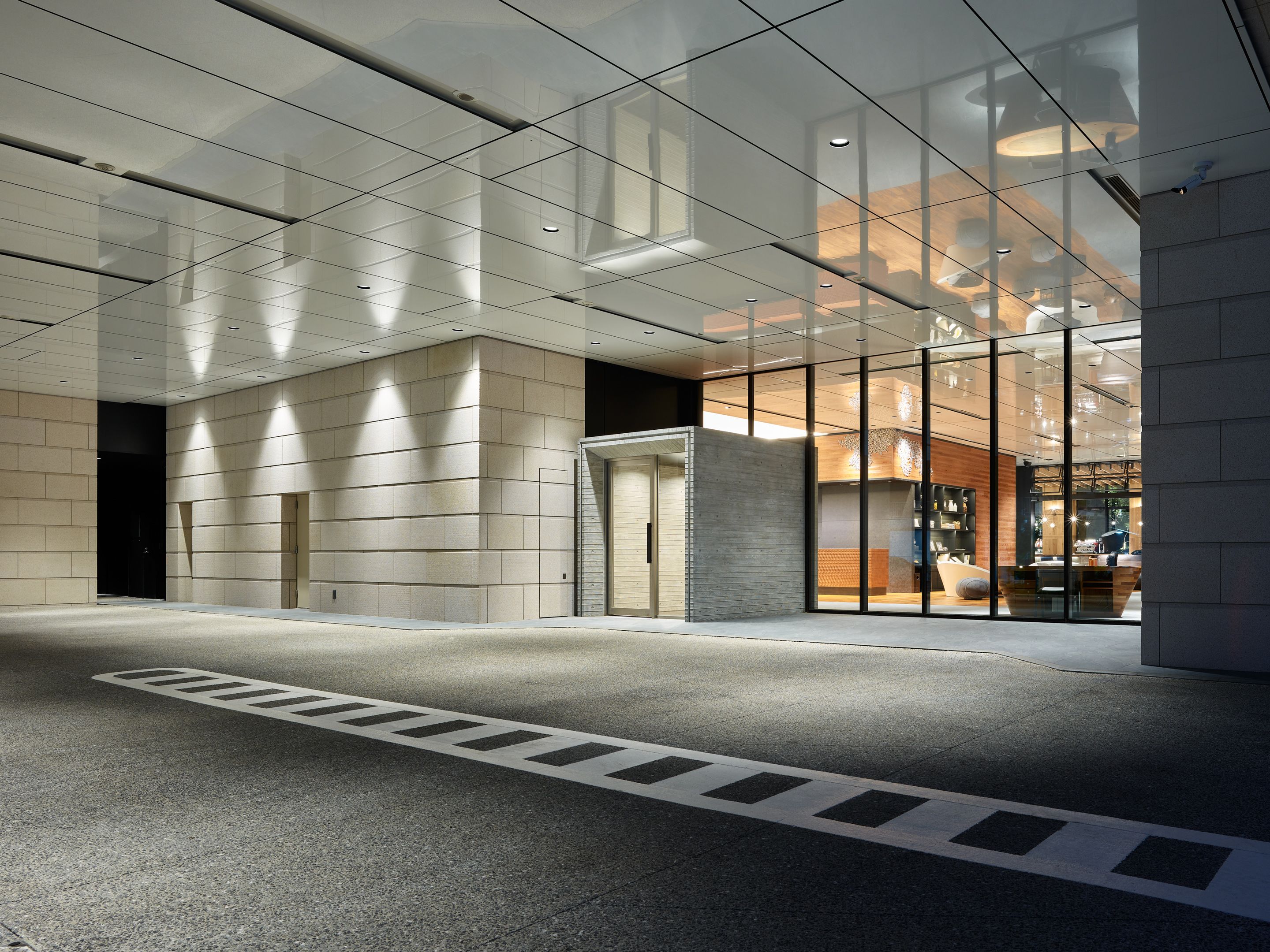 A modern building entrance with a glass facade, a concrete pillar, and a clear pedestrian pathway.
