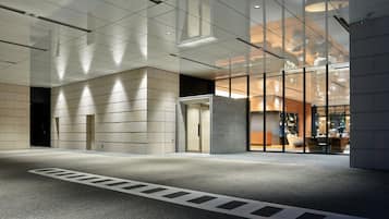 A modern building entrance with a glass facade, a concrete pillar, and a clear pedestrian pathway.