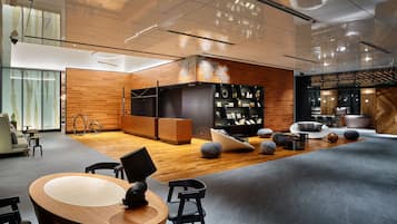A modern interior with a wooden reception desk, seating area, and a black shelving unit with various items.