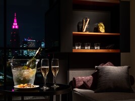 Une table avec des cocktails, des verres et des amuse-gueules, un canapé avec un coussin et une étagère avec des verres et une bouteille.