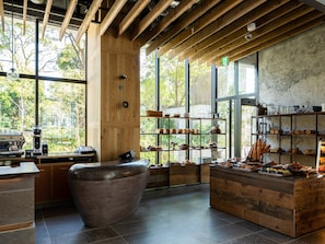 Interior de una cafetería con vigas de madera, un amplio espacio central con mesas y una variedad de productos horneados expuestos en estanterías.
