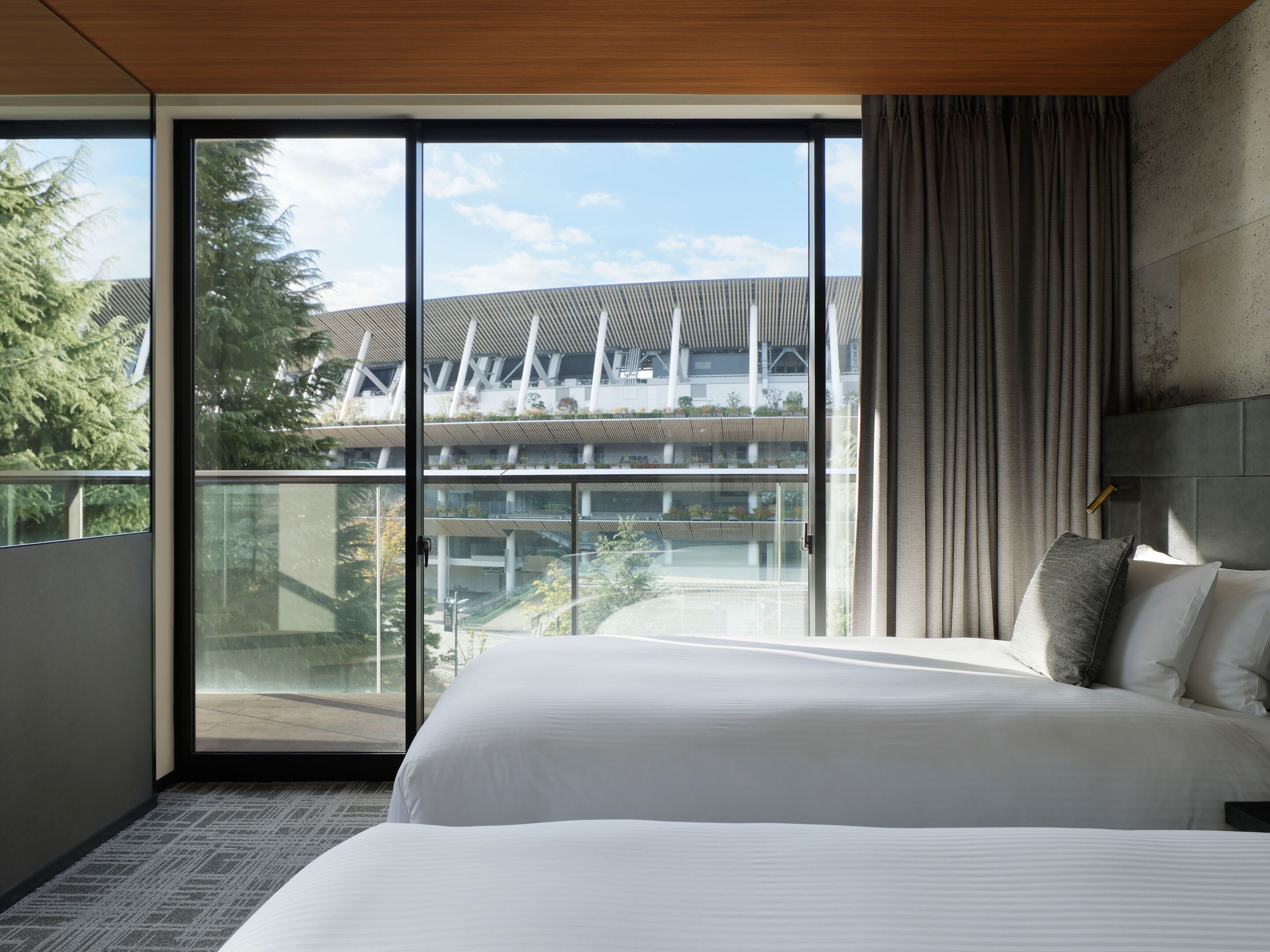 A modern hotel room with a large bed, a view of a building with a unique architectural design, and a balcony with a glass door.