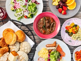 Un'ampia scelta di piatti, tra cui insalata, stufato e pasta, accompagnati da pane e dolci su un tavolo di legno.