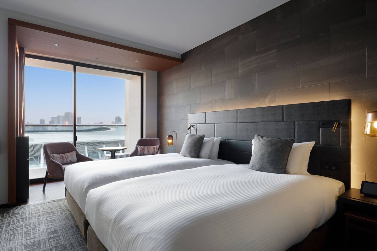 A modern hotel room with a large bed, a seating area, and a view of the city.