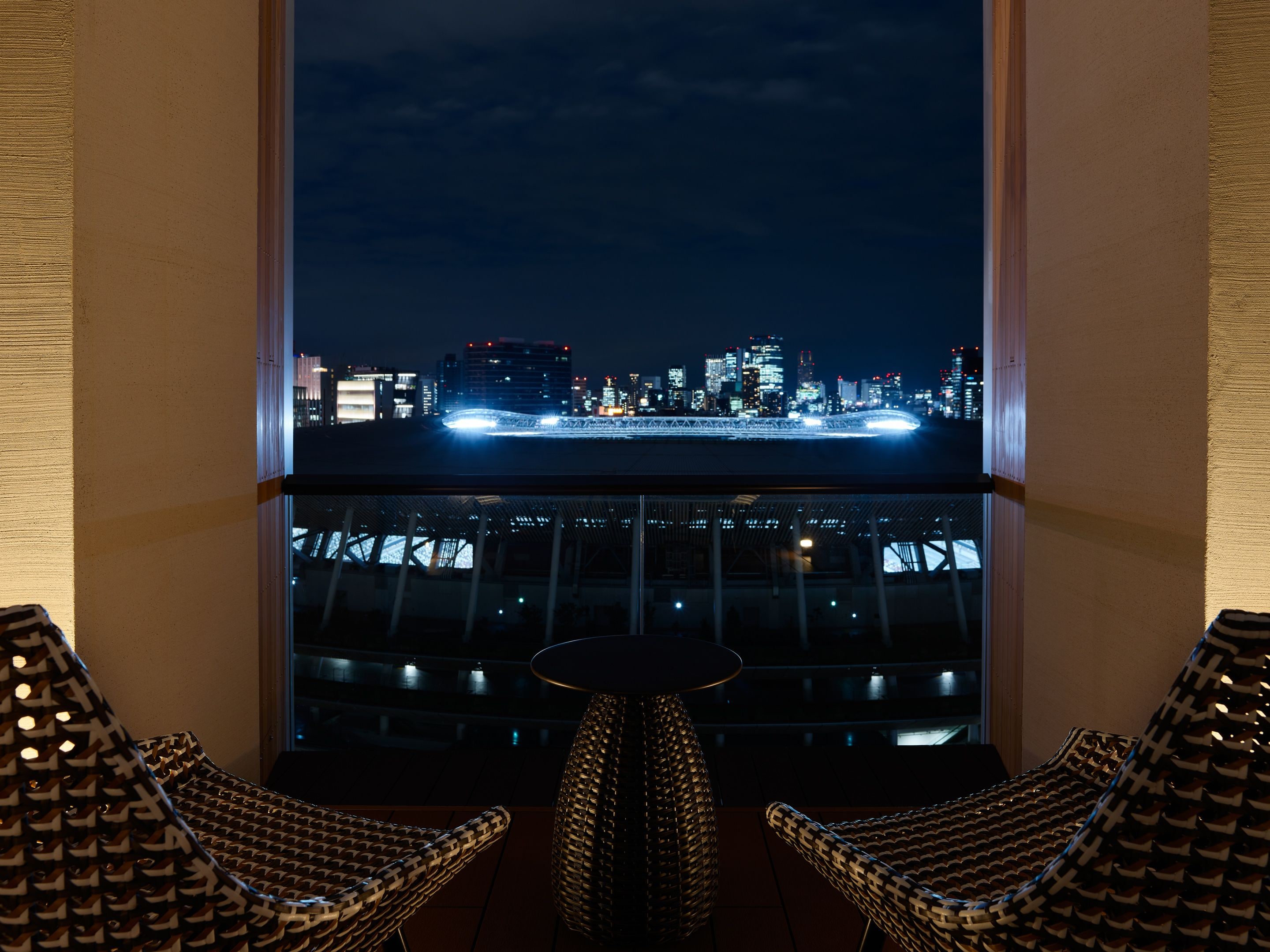 A balcony with a city view at night, featuring a table and two chairs.