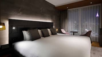 A modern hotel room with a large bed, a nightstand, a chair, a small table, and a city view through the window.