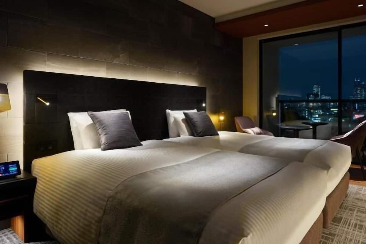 A modern hotel room with a large bed, a city view, and a small table with chairs.