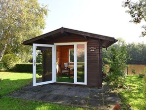 Uma pequena cabana de madeira com porta de vidro que dá para um pátio com mesa e cadeiras.