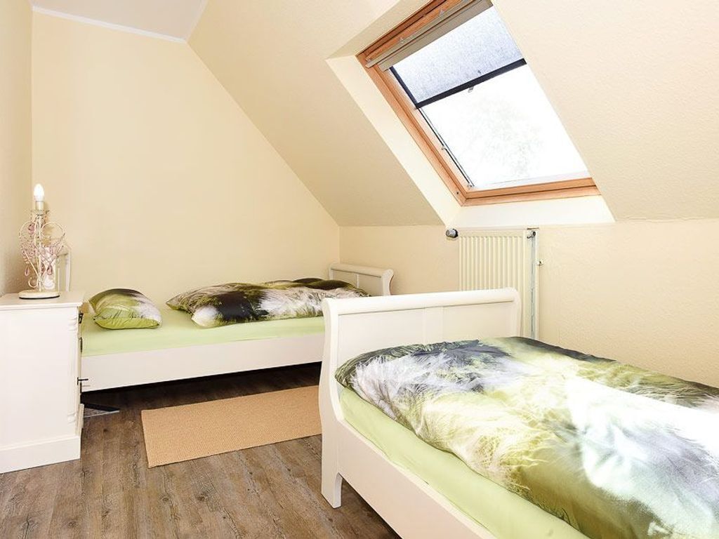 A small, well-lit room with a sloped ceiling, two beds with matching bedding, a radiator, and a skylight.