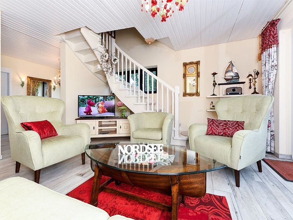 A living room with two armchairs, a glass coffee table, a staircase, and a television.