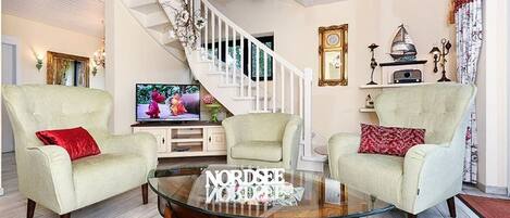 A living room with two armchairs, a glass coffee table, a staircase, and a television.