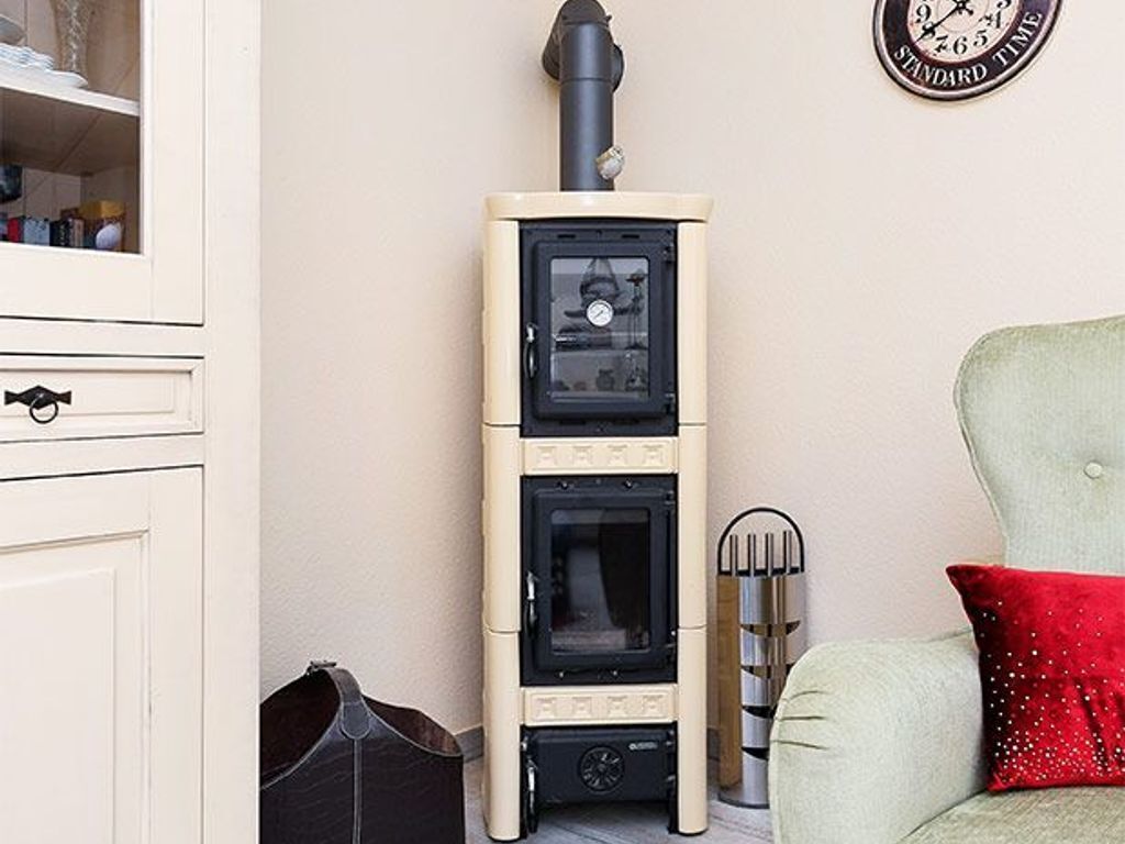 Een kamer met een beige muur, een wit kastje met een zwarte handgreep, een zwarte tas, een rood kussen op een lichtgroene stoel en een klok aan de muur.