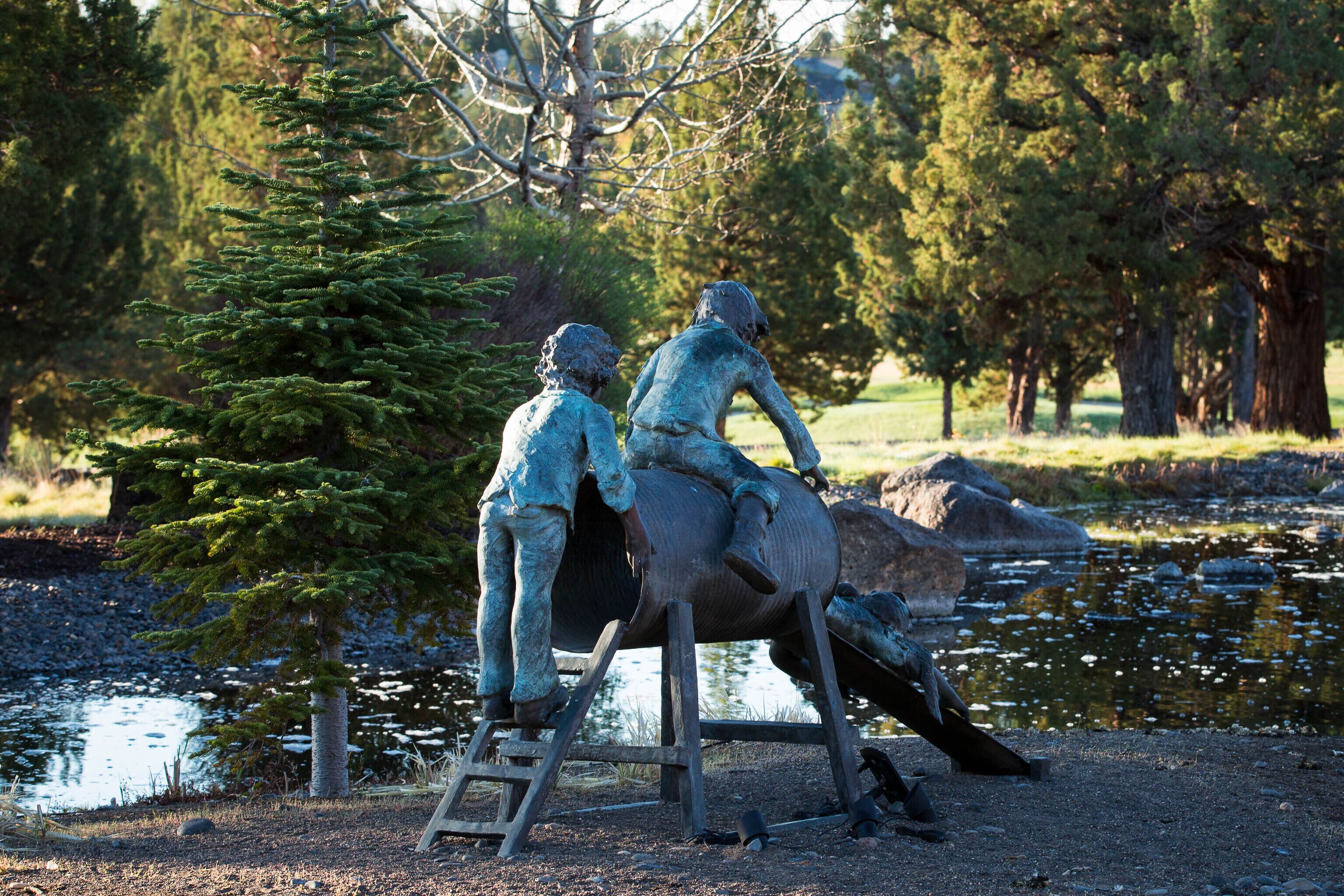 A sculpture of two figures on a wooden structure by a body of water, surrounded by trees.