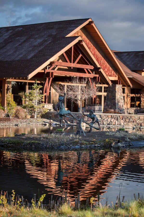 A lodge with a stone facade, wooden beams, and a pond with a sculpture.