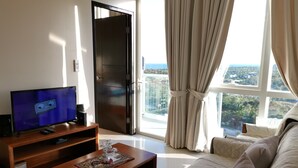 Ein modernes Wohnzimmer mit Fernseher, einem Holztisch, einer Couch und einem großen Fenster mit Vorhängen.