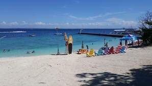 Ein Strand mit klarem türkisblauem Wasser, einer Mole und bunten Liegestühlen.