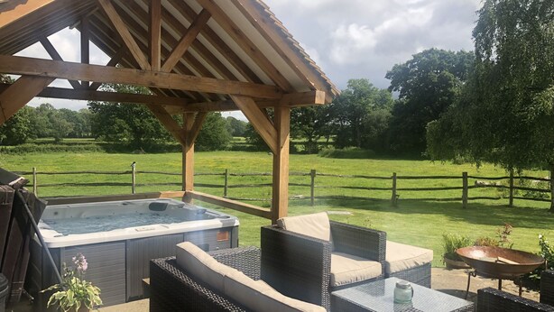 Un espacio de estar al aire libre techado con jacuzzi, mobiliario de mimbre y vistas a un campo cubierto de césped.