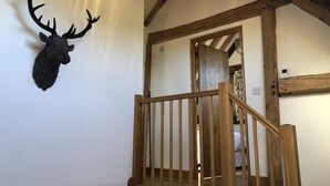 Una escalera con barandillas de madera lleva a un dormitorio con cama y una cortina blanca.