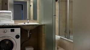 Un baño pequeño con lavadora, lavamanos y cabina de ducha de vidrio.