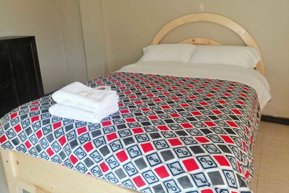 A single bed with a patterned bedspread, a wooden headboard, and a white pillow.
