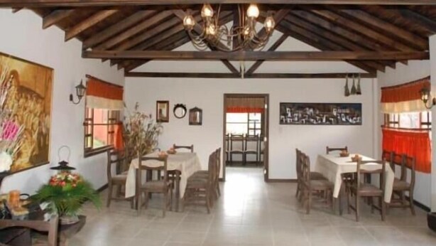 A dining area with wooden beams, a chandelier, and a large painting on the wall. - Hostería El Tisaleño (Tizaleo)