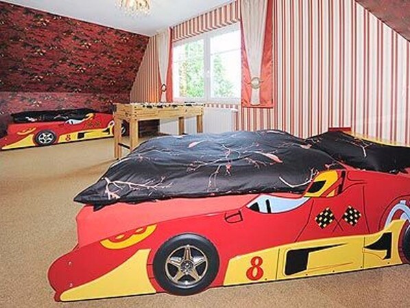 A room with a bed featuring a racing car design, striped curtains, and a window with natural light.