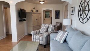 A living room with a striped armchair, a grey sofa, a glass coffee table, and a wooden cabinet. - Gorgeous Views of Harbor Entrance! Walk to town, east side location. (Boothbay Harbor)